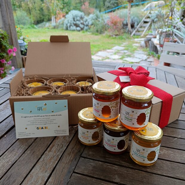 Immagine in esterno con una scatola regalo aperta e una confezionata con fiocco rosso. In primo piano, i 5 vasi di miele contenuti nella scatola "Calendula".